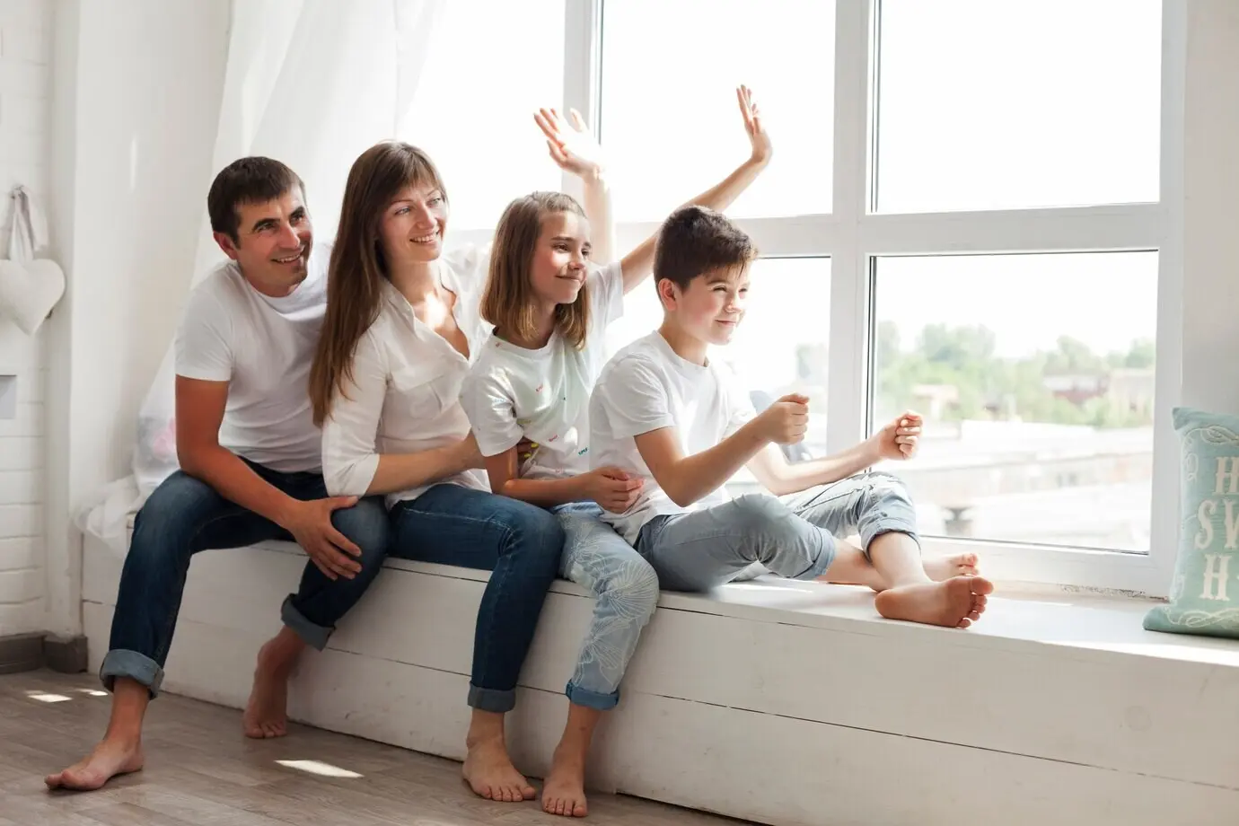 A smiling parent playing with their kids while sitting near a window.